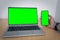 Mockup image of a man holding a mobile phone with green screen and a laptop with blank green screen on table