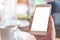 Mockup image of a woman`s hand holding white mobile phone with blank desktop screen and coffee cup