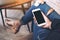 Mockup image of a woman sitting cross legged , holding white mobile phone with blank black desktop screen on thigh