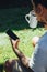 Mockup shot of man`s hand with tattoos holding  cell phone and coffee cup with blank screen in backyard