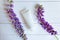 Mockup of unbranded white bottle tube for branding and purple flowers on white wooden table with horizontal boards. Top view