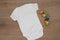 Mockup of white baby bodysuit on wood background with colorful toy. Blank baby clothes template mock up, flat lay styled stock