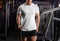 Mockup of a white sports t-shirt on a sports guy in the gym, against the background of inventory, training clothes, front view