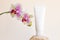 Mockup white squeeze bottle cosmetic tube on rock, phalaenopsis orchid flowers on beige background. Body cream, gel, skin care,