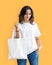 Mockup of a woman posing with blank white tote bag and shirt summer themed orange background