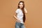 Model girl with slim body in a white t-shirt posing with one hand in pocket at the beige background, isolated. Clothes