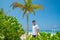 Model handsome young guy in white t-shirt standing on sandy beach at tropical island luxury resort