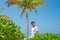 Model handsome young man in white t-shirt standing on sandy beach at tropical island luxury resort