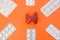 Model of thyroid gland surrounded by six blister packs with white pills inside in corners of image on orange background. Photo co