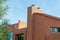 Modern adobe style building with orange exterior cement stucco with windows and front yard trees