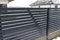 Modern anthracite panel fencing with a visible connector of the fence foundations, it rains in winter, in the background the roofs