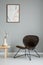 Modern armchair next to wooden table with flowers in grey interior with poster on the wall.