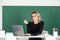 Modern attractive teacher. Portrait of smart young woman in glasses with book on the blackboard in class at high school