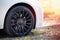 Modern auto wheel of car with beautiful black alloy disc and fresh rubber tread on rustic forest road with green grass on sunset