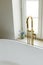 Modern bathroom with stylish golden faucet, white bathtub and travertine tiles. Stylish bathroom details with summer flowers