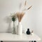 Modern beige ceramic vases with dry grass branches on white table near a black white wall backdrop. Copy space.Minimal Scandinavia