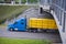 Modern blue semi truck with yellow cover cargo on trailer flat b