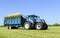 Modern blue tractor pulling a trailer in grass field