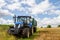 Modern blue tractor pulling a trailer in harvest field