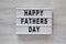 Modern board with `Happy Fathers Day` words over white wooden surface, top view. Overhead, from above, flat lay. Close-up