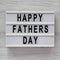 Modern board with `Happy Fathers Day` words over white wooden surface, top view. Overhead, from above, flat lay. Close-up