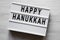 Modern board with `Happy Hanukkah` word over white wooden background, top view. From above, flat-lay