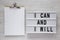 Modern board with `I can and I will` words, clipboard with blank sheet of paper on a white wooden surface, top view