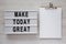 Modern board with `Make today great` words, clipboard with blank sheet of paper on a white wooden surface, top view. Flat lay