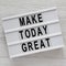 Modern board with `Make today great` words on a white wooden table, top view. Overhead, from above. Flat lay