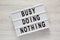 Modern board with text `Busy doing nothing` on a white wooden surface, top view. From above, flat lay, overhead. Close-up