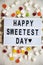 Modern board with text `Happy Sweetest Day` word and candy over white wooden background, top view. From above, flat lay, overhea