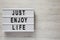 Modern board with text `Just enjoy life` on a white wooden background, top view. Copy space