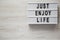 Modern board with text `Just enjoy life` on a white wooden surface, top view. Copy space