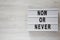 Modern board with text `Now or never` word on modern board on a white wooden surface, top view. Copy space