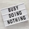 Modern board with words `Busy doing nothing` on a white wooden background, top view. From above, flat lay, overhead. Close-up