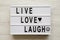 Modern board with words `Live Love Laugh` over white wooden background, top view. Flat lay, overhead