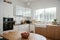 Modern bright kitchen interior with white horizontal window blinds, wooden cabinets with white countertop and household appliances