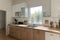 Modern bright kitchen interior with white horizontal window blinds, wooden cabinets with white countertop and household appliances