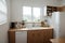 Modern bright kitchen interior with white horizontal window blinds, wooden cabinets with white countertop and household appliances