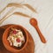 Modern brown silicone bowl of granola with yogurt, nuts and pair of ripe raspberries served on wooden tray with spoon.