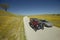 A modern car driving by a maroon Model T on a scenic road surrounded by spring flowers off of Route 58, Shell Road, CA