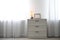 Modern chest of drawers with lamp near window