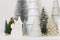 Modern christmas scene, miniature snowy village on white table. Merry Christmas! Stylish little Christmas trees and house