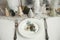 Modern Christmas table setting. Cedar branch with bell on plate, vintage cutlery, glasses, festive little christmas trees and