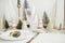 Modern Christmas table setting. Cedar branch with bell on plate, vintage cutlery, glasses, festive little christmas trees and