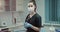 Modern clinic room young nurses assistant with a surgical mask on the face looking straight to the camera and holding a