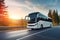 Modern coach bus speeds along a scenic highway, winding through a forest with a beautiful sunset countryside backdrop