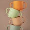 Modern colorful pastel silicone cups stacked in column on brown background. Baby tableware, first feeding.