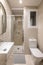 Modern compact beige tiled bathroom with glass walk-in shower, sink and mirror and white toilet with window. Concept of