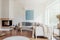 Modern corner fireplace in a sunny, peaceful living room interior with white walls and cozy pillows and blankets on a beige sofa.